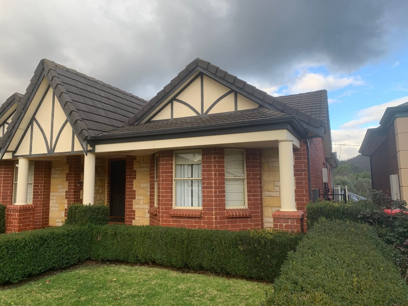 A restored tiled roof on a brick home with a hedge in front.