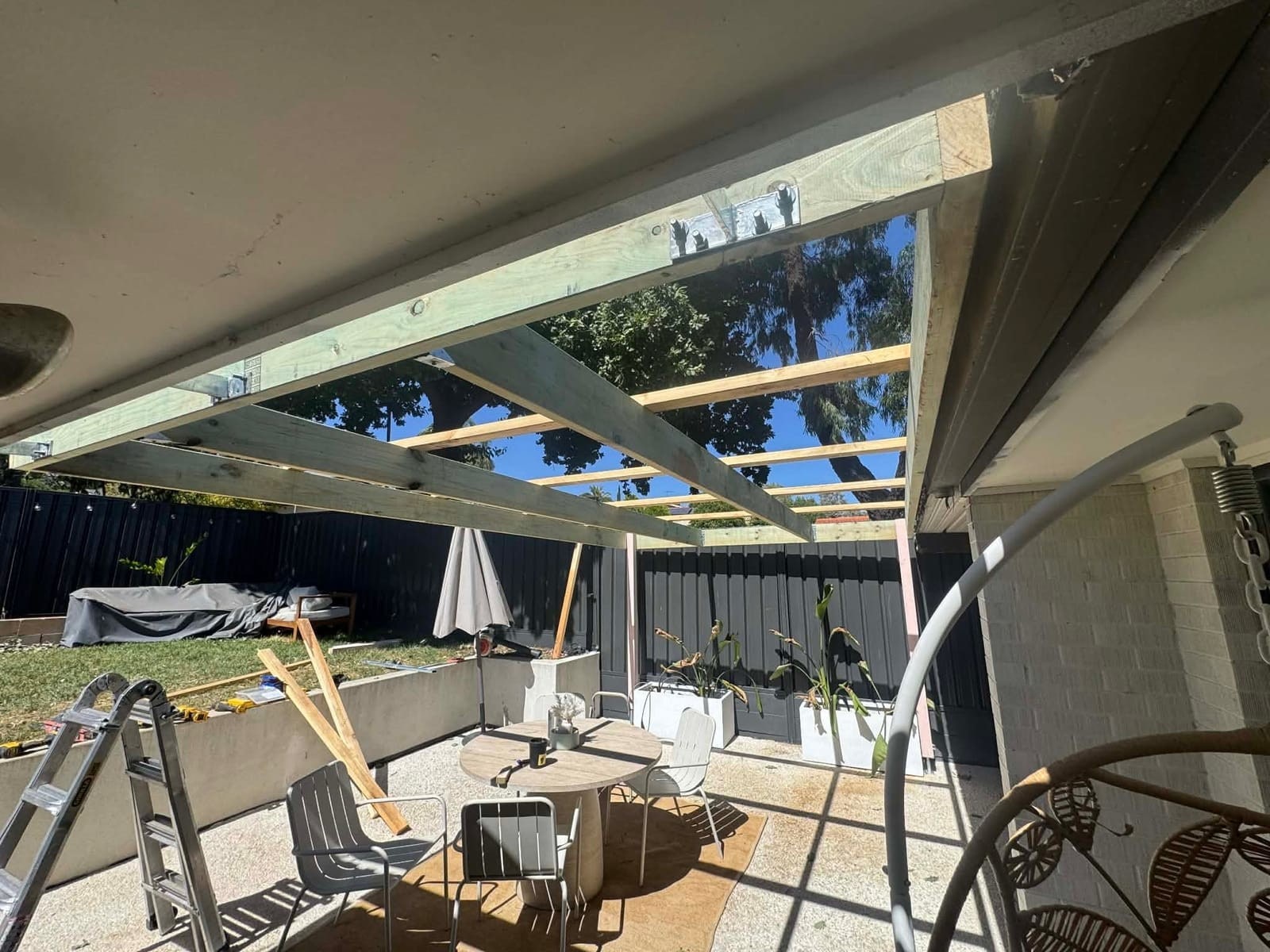 A pergola roof frame going up over a backyard.