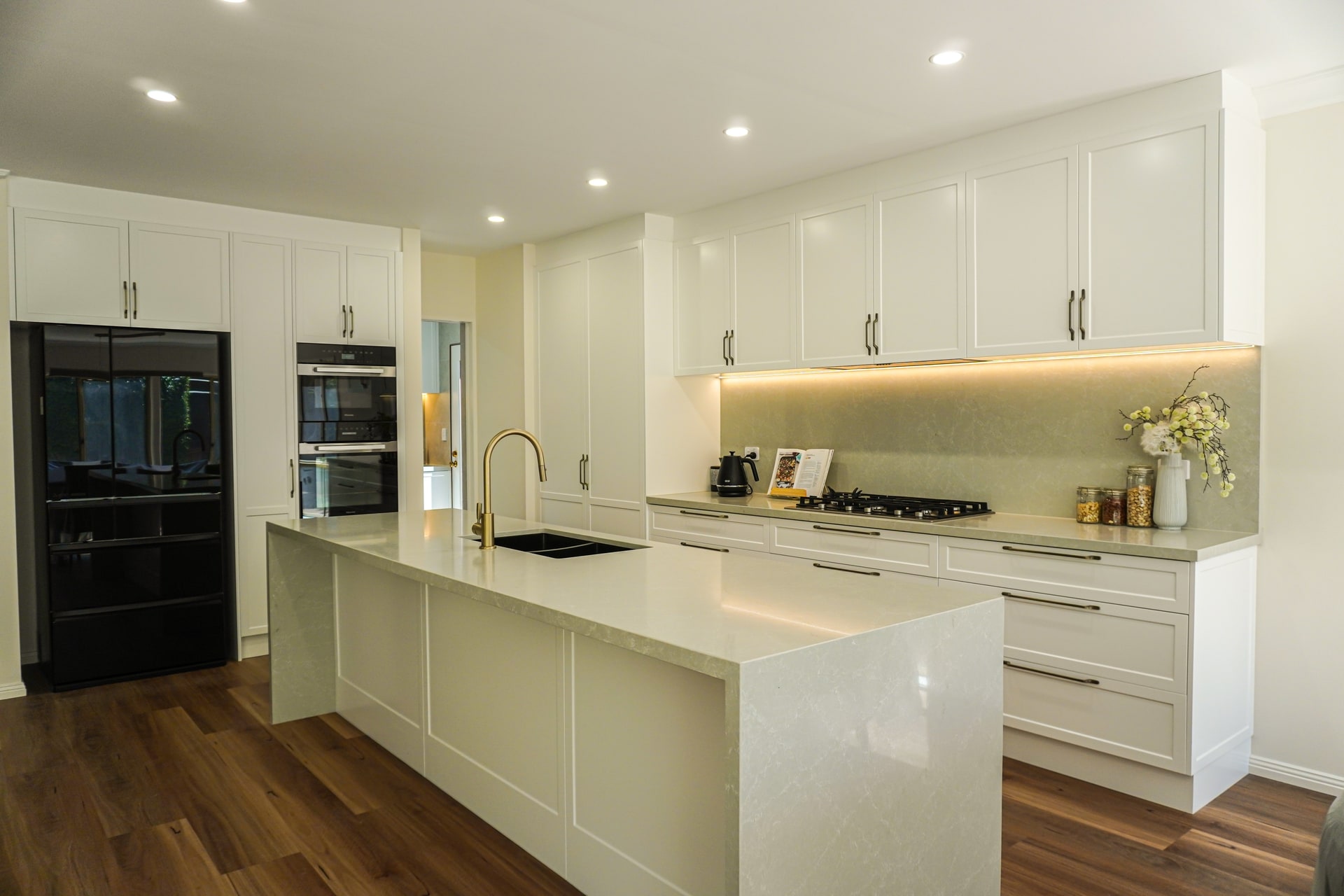 A finished Torrens Park kitchen by ASP Build & Co: a long stone island, white shaker cabinets and LED strip lighting.