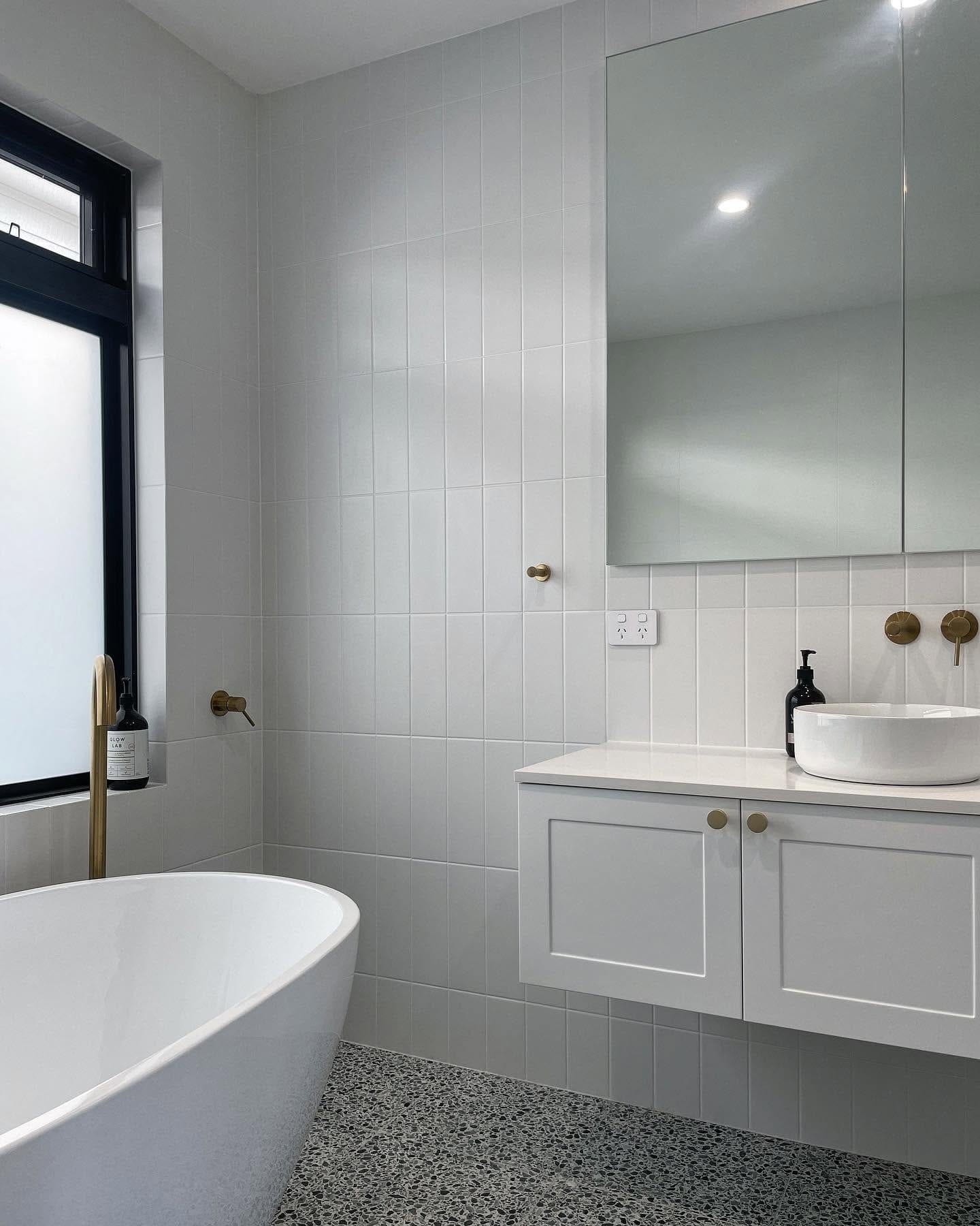 A white Becks bathroom with brass tapware and a terrazzo floor.