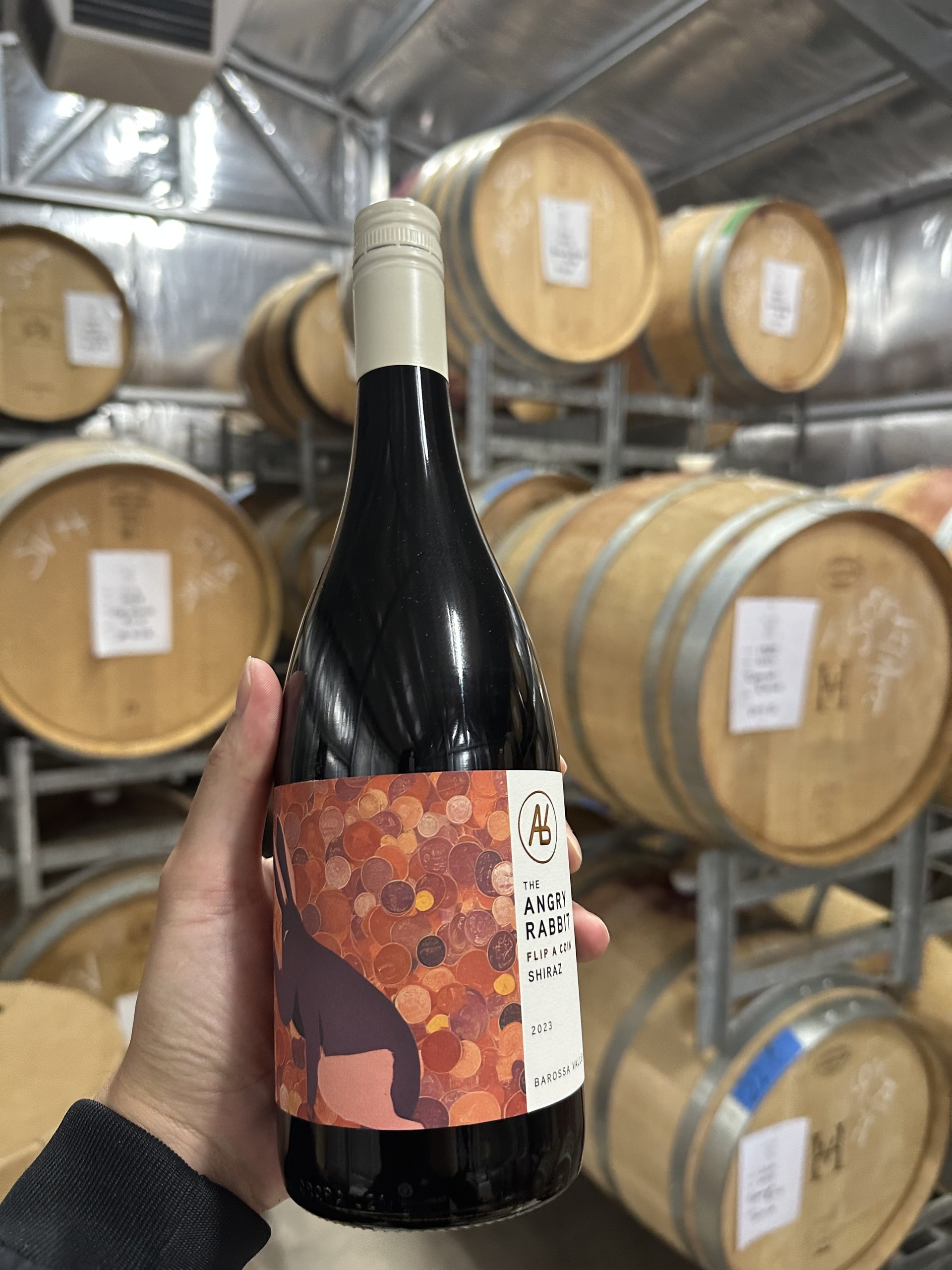 A bottle of The Angry Rabbit wine held up in a barrel room.
