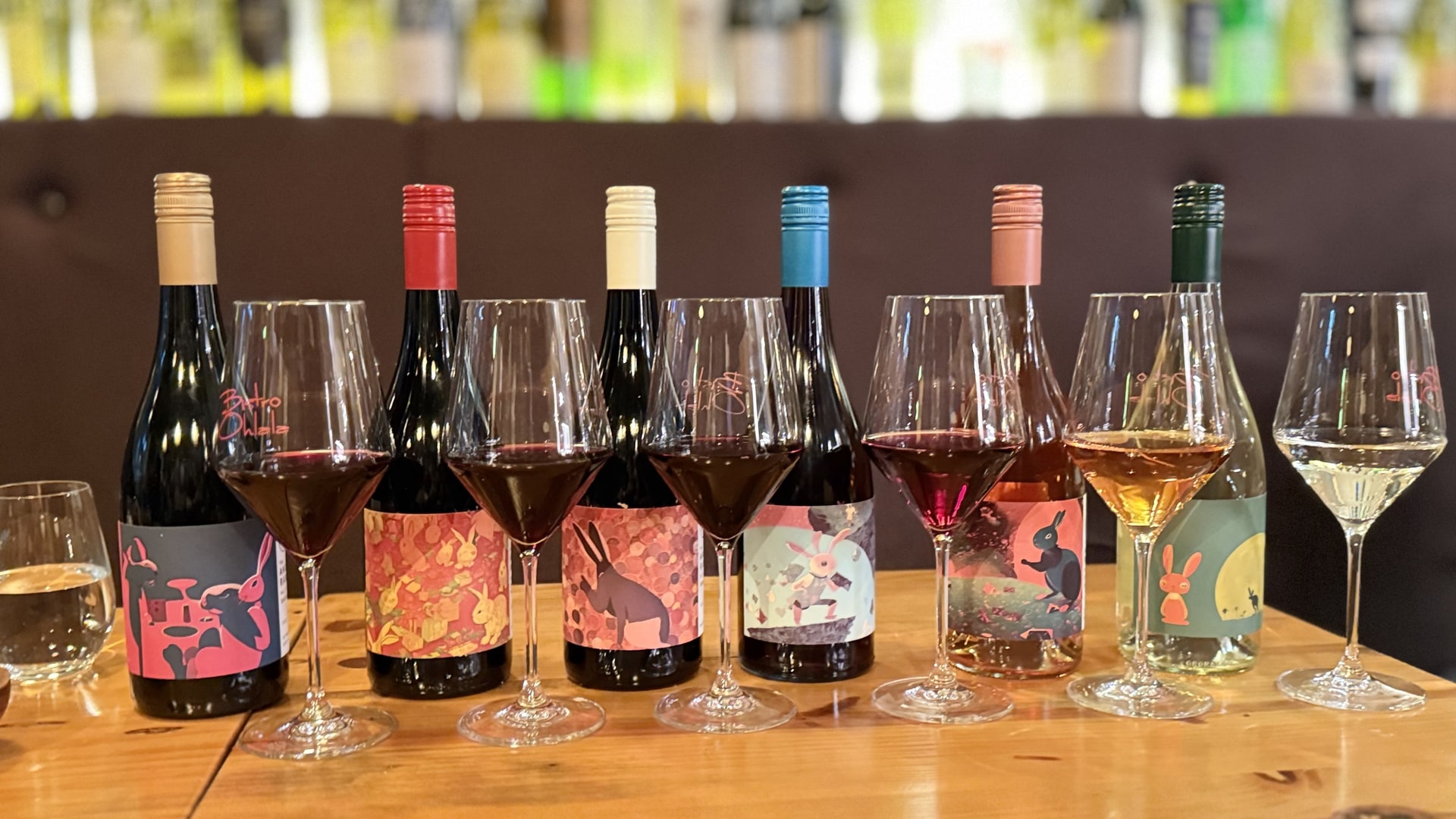 A line-up of The Angry Rabbit wines with filled glasses on a bar.