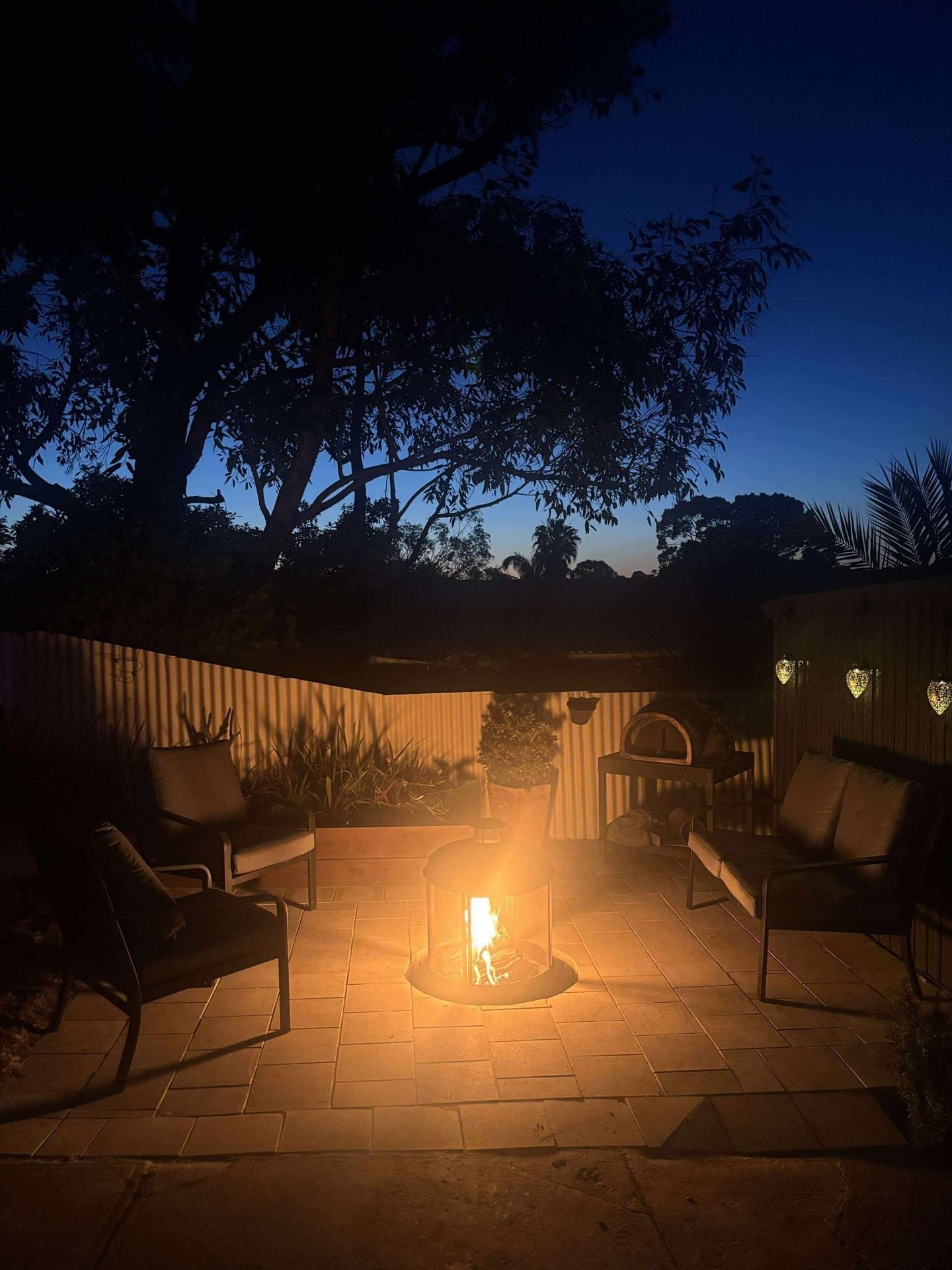 A paved backyard entertaining area with a lit fire pit at dusk, from May Paving’s own job photos.