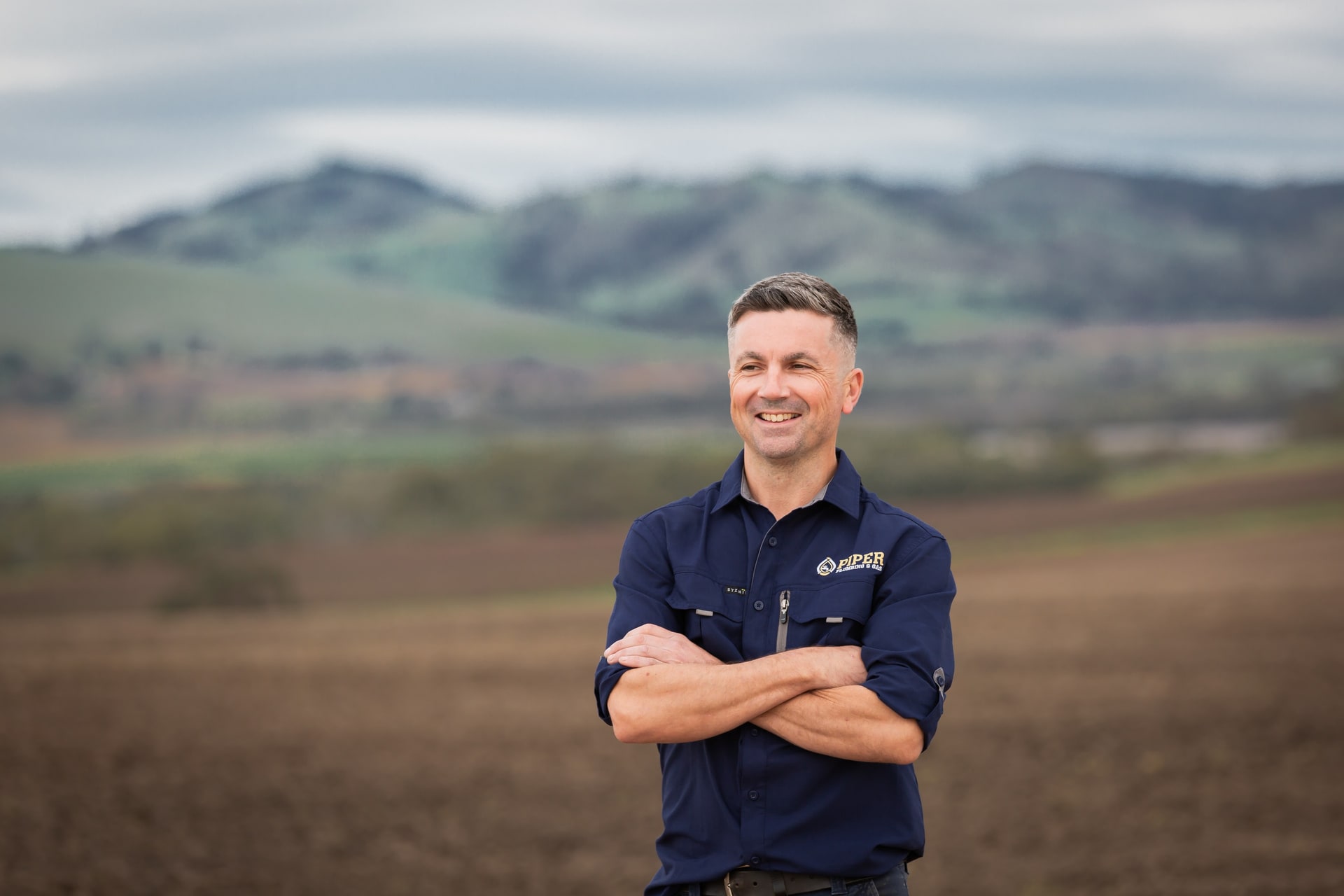 Craig from Piper Plumbing & Gas, arms crossed, in a Barossa paddock.