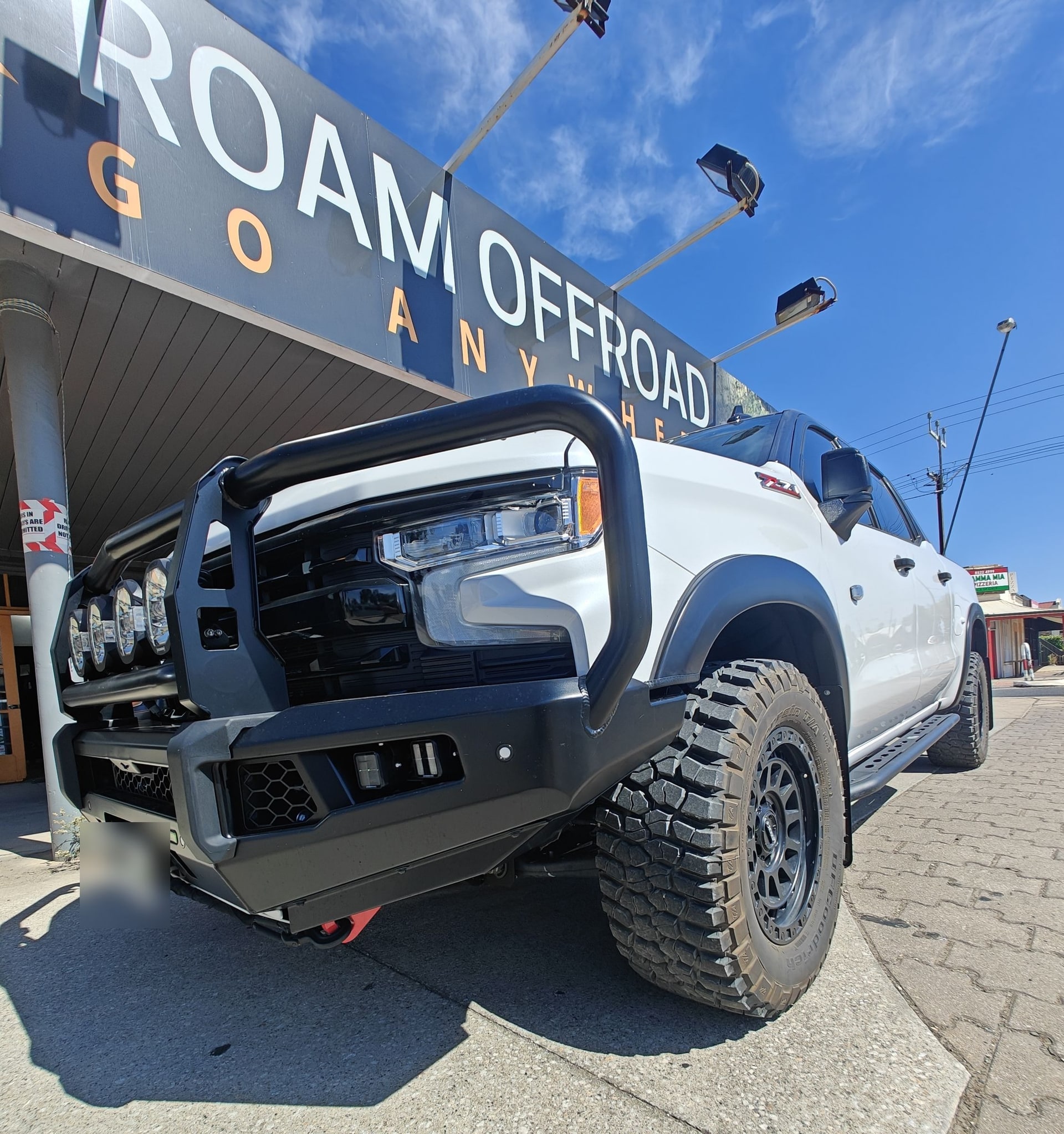 A white Chevrolet Silverado fitted with an Ironman 4x4 bull bar, under the Roam Offroad sign in Gawler South.