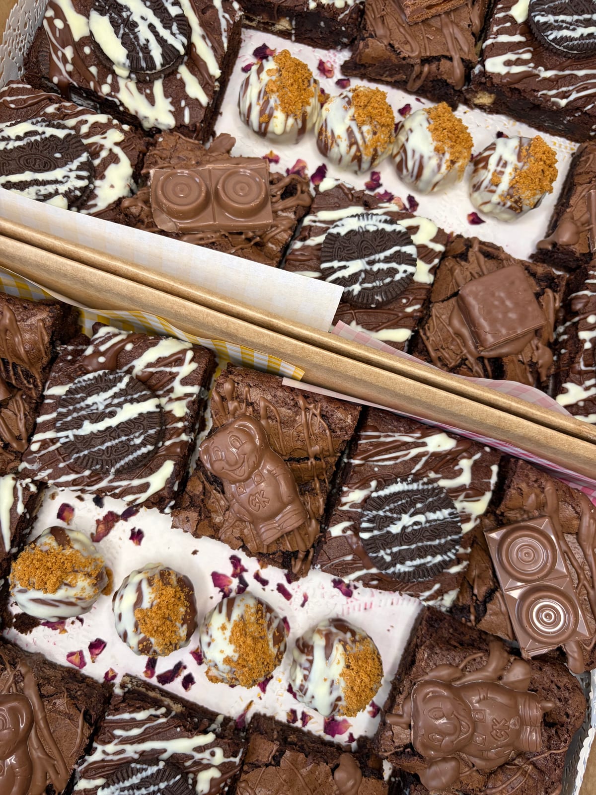 A grazing box of Auggies Kitchen brownies and chocolate slices drizzled with white chocolate, with a pair of wooden tongs.
