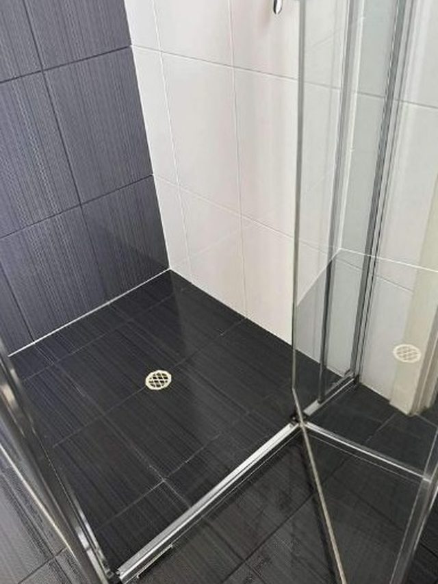 A shower recess after a Barossa Valley Cleaning Services clean: dark floor tiles wiped clear, white wall tiles and a clean glass screen.