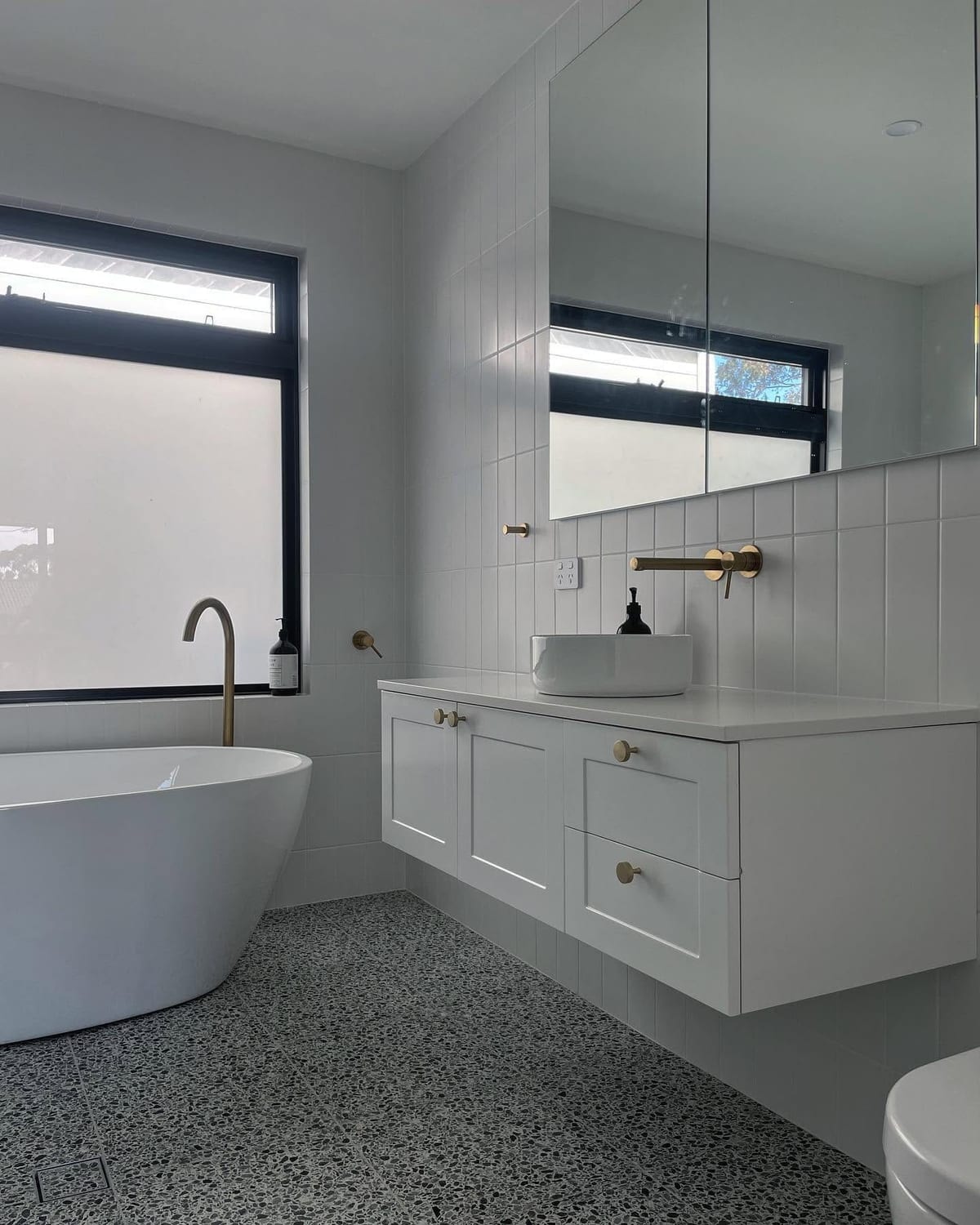 A finished bathroom in Flagstaff Hill with terrazzo flooring, a freestanding bath, white vanity and brushed brass tapware.