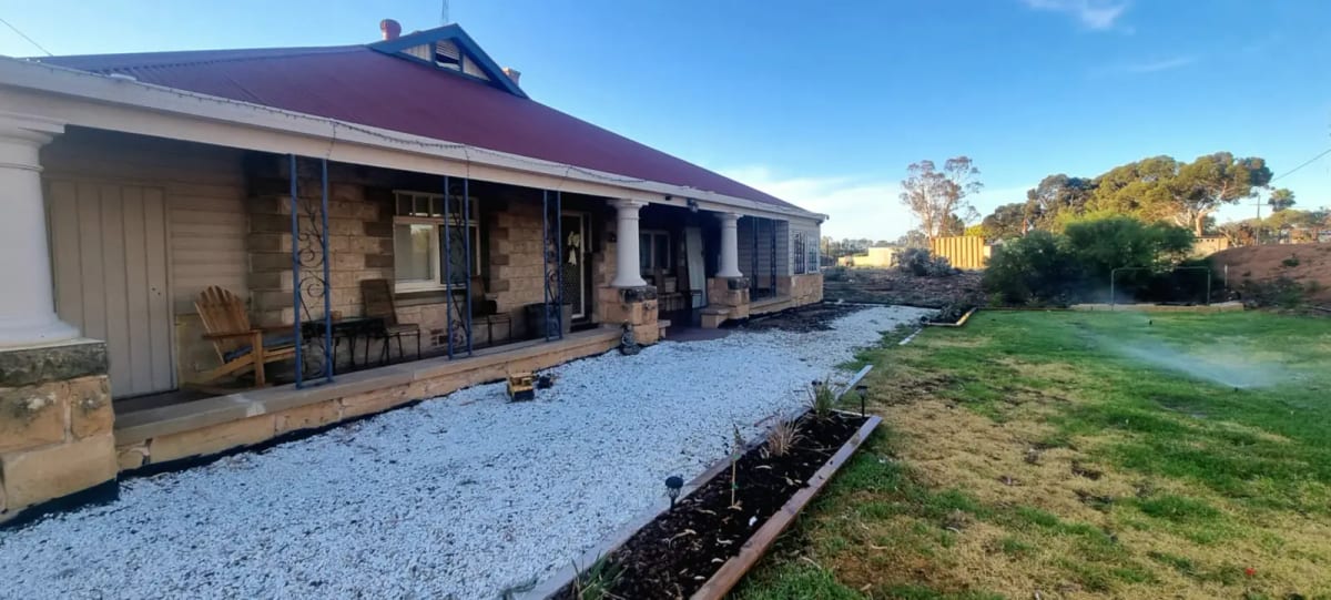 A stone homestead verandah with a new white gravel path and an edged garden bed laid alongside it.