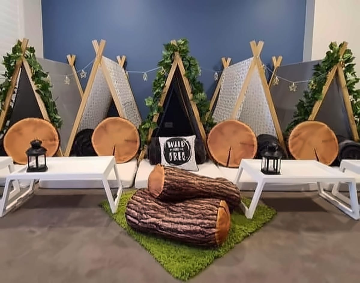 A Wild Nights jungle teepee setup with leafy garlands, round log cushions and a fake-grass rug.
