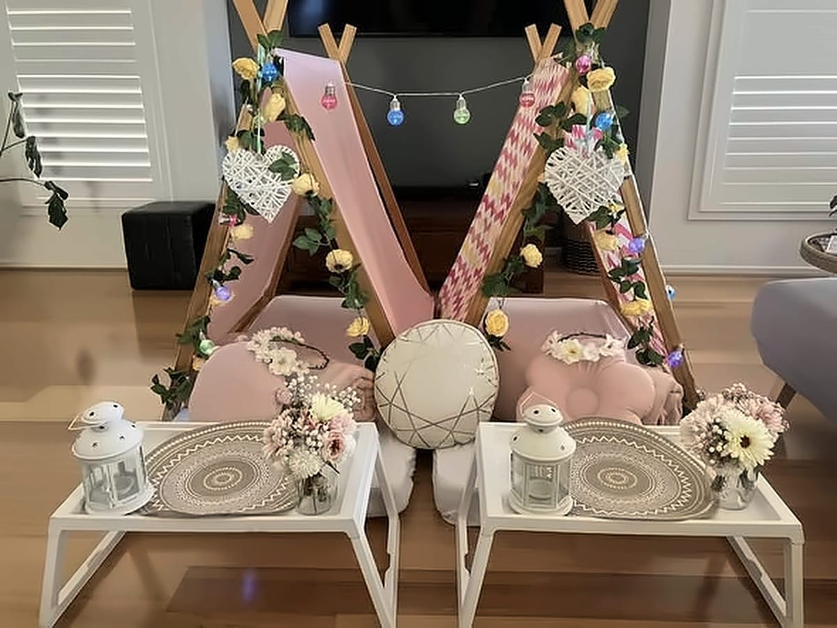 A Boho teepee setup with pink chevron teepees, flower garlands, heart cushions, lanterns and white tray tables.
